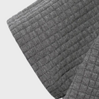 Gros plan sur un tissu gaufré gris, texture en relief, idéal pour vêtements d'hiver ou décoration intérieure. Matériau doux et confortable.