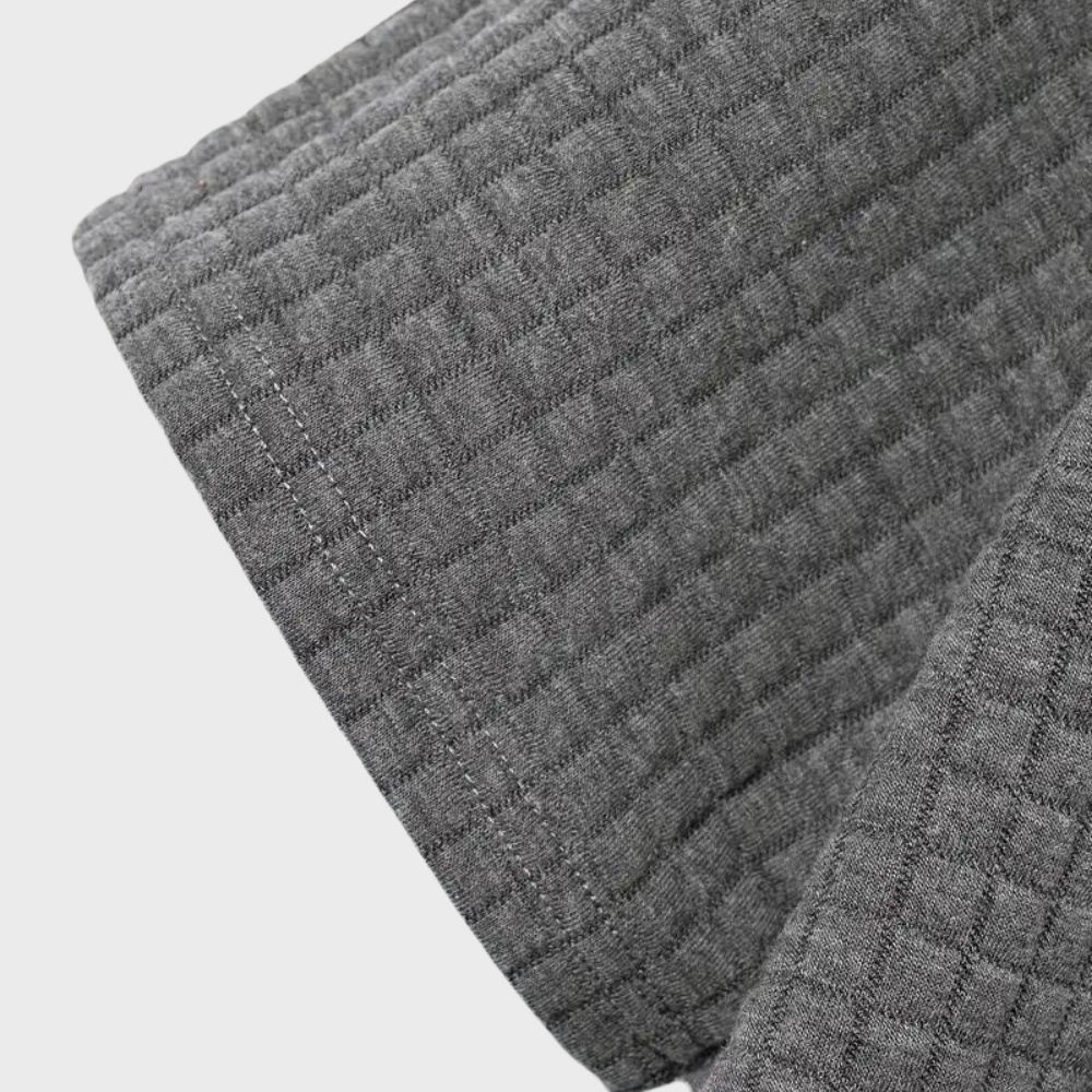 Gros plan sur un tissu gaufré gris, texture en relief, idéal pour vêtements d'hiver ou décoration intérieure. Matériau doux et confortable.