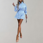 Femme en combishort bleu en dentelle, manches longues, talons nus, fond neutre. Mode féminine élégante, tenue estivale tendance.