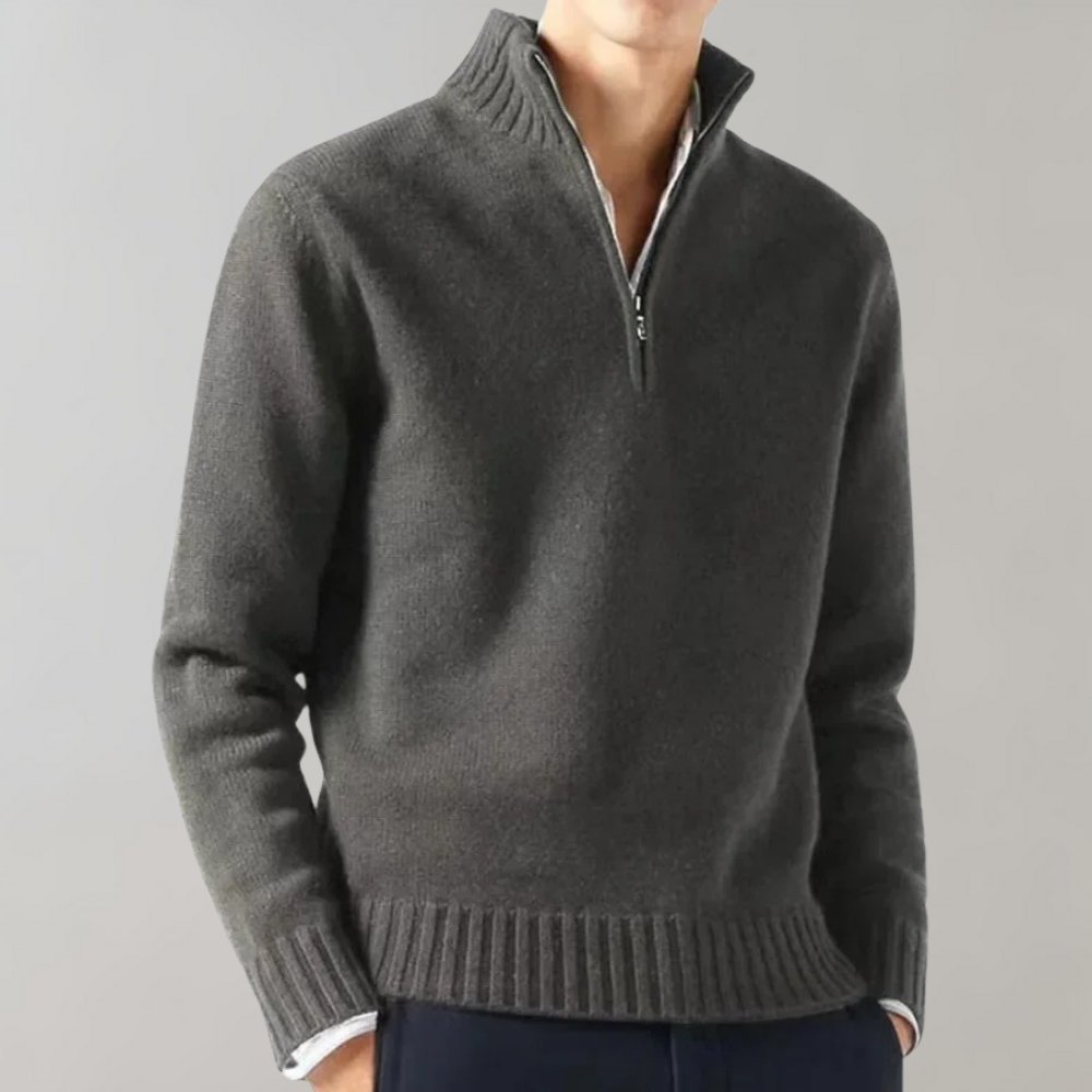 Homme portant un pull gris à col zippé, manches longues, sur fond gris. Mode masculine élégante, pull-over chaud pour l'hiver.