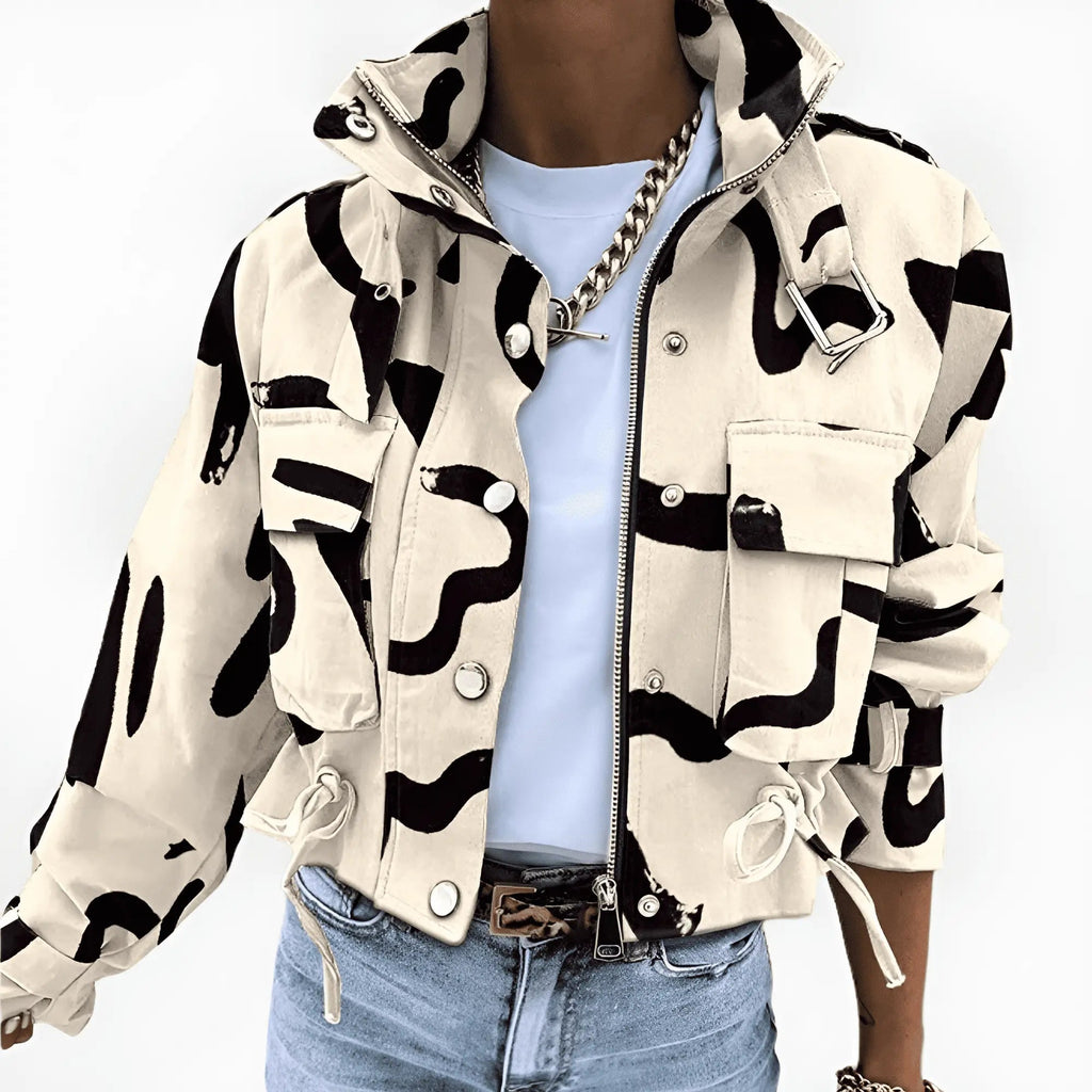 Veste camouflage beige et noire, style militaire, avec poches et cordons, portée par une personne en jean et t-shirt blanc. Mode urbaine tendance.