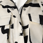 Veste en jean motif vache noir et blanc, fermeture éclair argentée, poches à rabat, style tendance et moderne, mode urbaine chic.