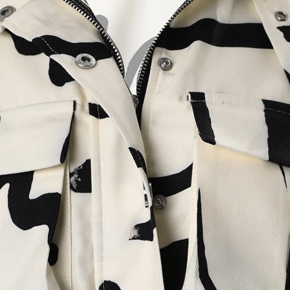 Veste en jean motif vache noir et blanc, fermeture éclair argentée, poches à rabat, style tendance et moderne, mode urbaine chic.