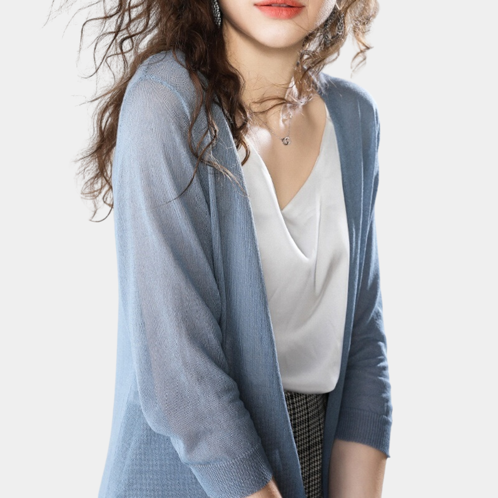 Femme portant un cardigan bleu léger sur un top blanc, cheveux bouclés, style décontracté chic, mode féminine élégante, fond blanc.