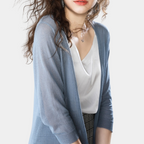 Femme portant un cardigan bleu léger sur un top blanc, cheveux bouclés, style décontracté chic, mode féminine élégante, fond blanc.