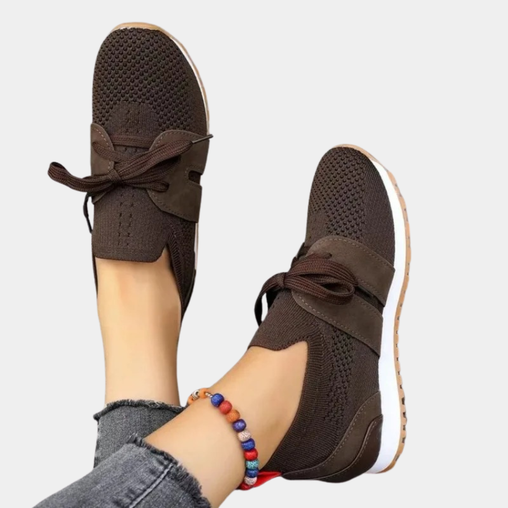 Chaussures marron en maille respirante avec lacets, portées par une personne avec un bracelet coloré, sur fond blanc. Sneakers confortables et tendance.
