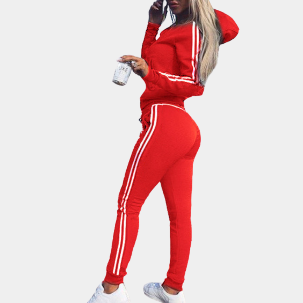 Femme en survêtement rouge à capuche avec rayures blanches, tenant un gobelet. Mode sportive, tenue décontractée, style urbain tendance.