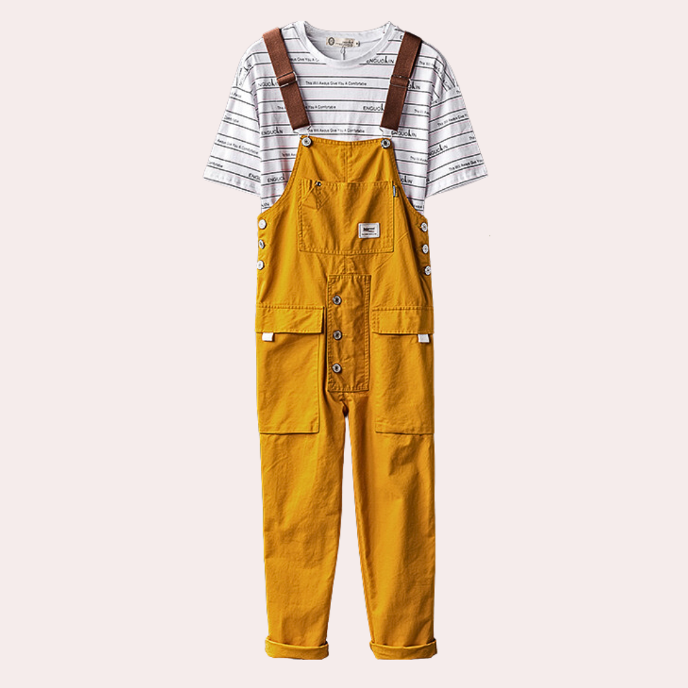 Salopette jaune moutarde avec boutons, poches avant, bretelles marron, portée sur un t-shirt rayé blanc et noir. Mode enfant tendance.