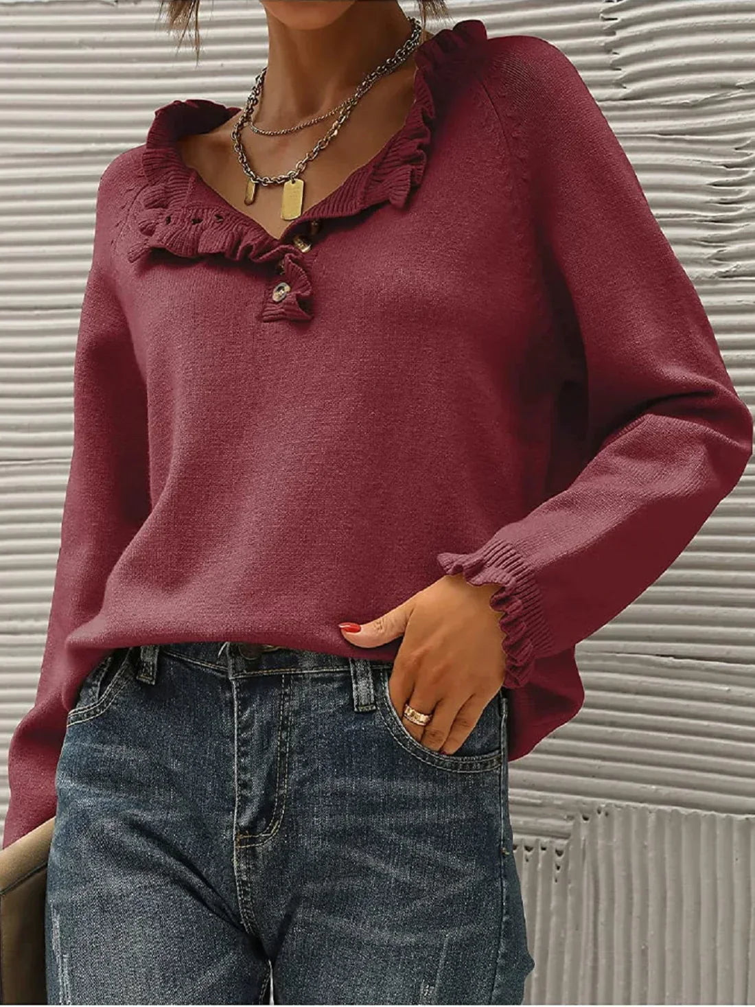 Femme portant un pull bordeaux à col en V avec volants, associé à un jean bleu. Mode automne, style décontracté, tendance féminine.