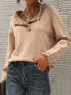 Femme portant un pull beige à volants avec un col en V, associé à un jean bleu. Style décontracté chic, mode automne-hiver tendance.