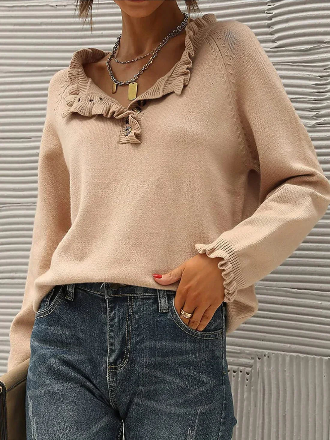 Femme portant un pull beige à volants avec un col en V, associé à un jean bleu. Style décontracté chic, mode automne-hiver tendance.
