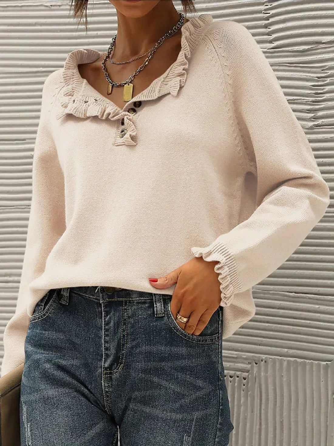 Femme portant un pull beige à volants avec col en V, associé à un jean bleu. Style décontracté et élégant, idéal pour l'automne.