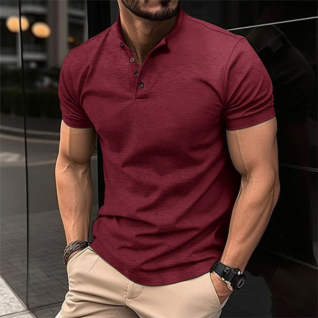 Homme portant un polo rouge élégant, manches courtes, avec montre noire et bracelets, debout en extérieur urbain. Mode masculine moderne.