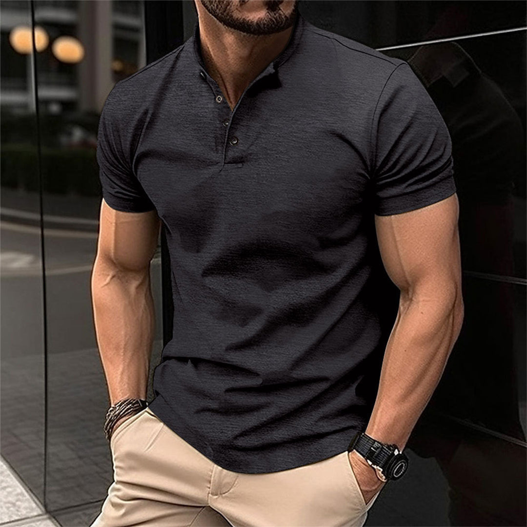 Homme musclé portant un polo noir ajusté et un pantalon beige, montre noire au poignet, debout en extérieur urbain moderne.