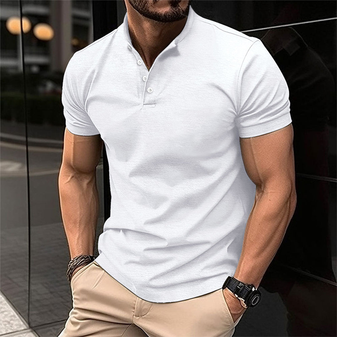 Homme musclé portant un polo blanc ajusté, debout en extérieur urbain. Mode masculine, style décontracté chic, montre-bracelet noire.