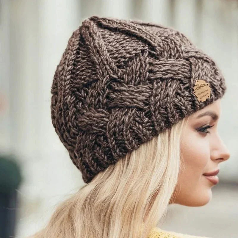 Femme portant un bonnet en laine tricoté marron, motif tressé, étiquette en cuir, style hiver, mode féminine, accessoire chaud et tendance.