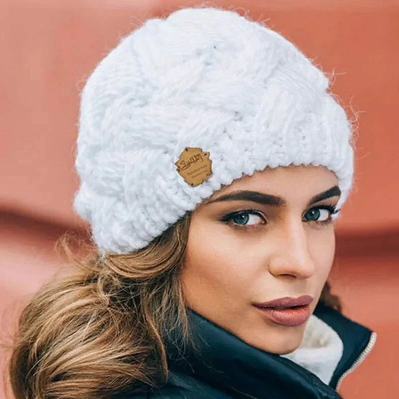 Femme portant un bonnet en laine blanc tricoté, style hivernal, avec étiquette en cuir. Mode hiver, accessoires chauds, tendance féminine.