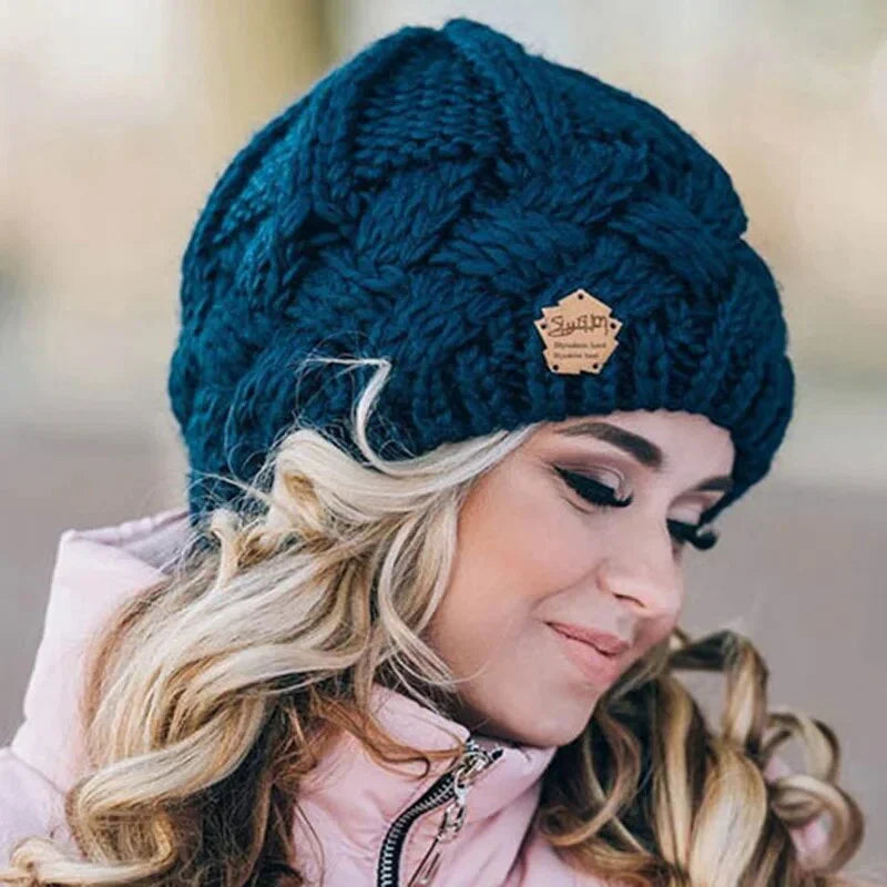 Femme portant un bonnet en laine bleu foncé tricoté, cheveux blonds bouclés, veste rose. Mode hiver, accessoires chauds, style élégant.