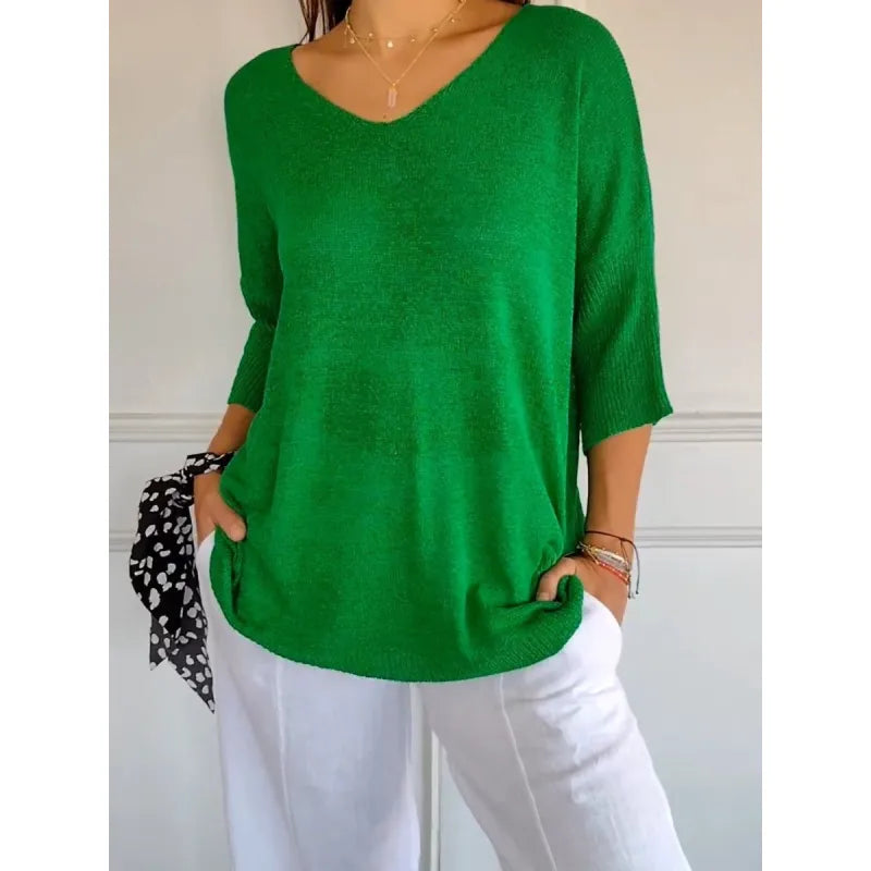 Femme portant un pull vert ample à col en V, manches trois-quarts, avec un pantalon blanc. Mode décontractée, tendance printemps-été.