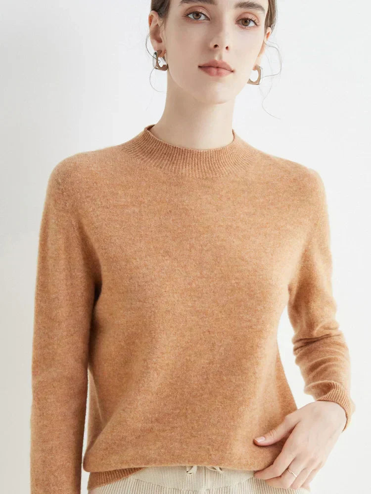 Femme portant un pull en cachemire beige, manches longues, col rond, posant contre un fond blanc. Mode automne-hiver, style élégant et minimaliste.