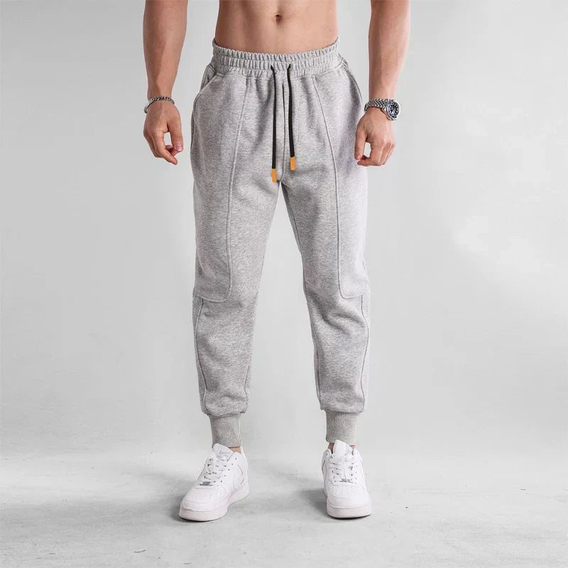 Pantalon de jogging gris pour homme, coupe ajustée, avec cordon de serrage, poches latérales, porté avec baskets blanches. Mode décontractée tendance.