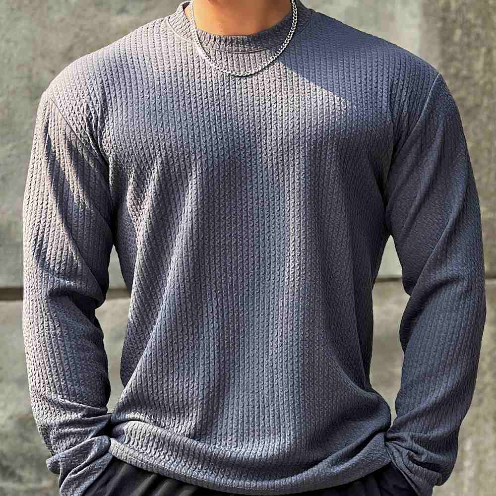 Homme portant un pull gris texturé à manches longues, chaîne argentée visible. Mode masculine, style décontracté, tendance automne-hiver.