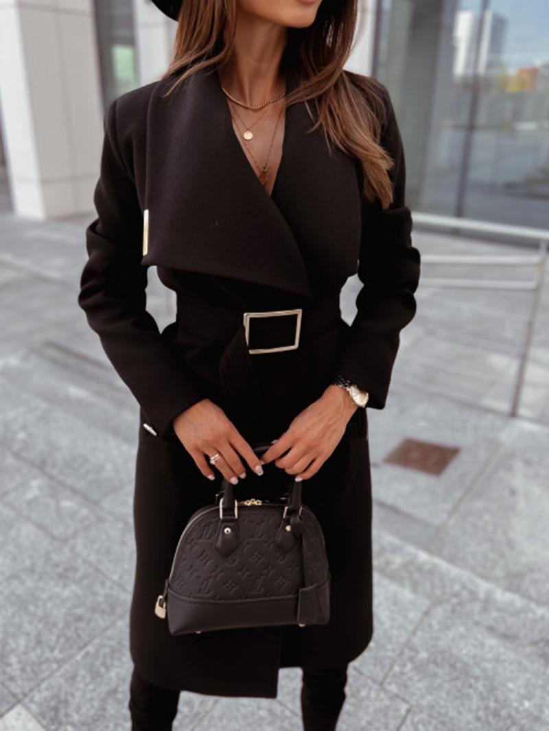 Femme élégante en manteau noir ceinturé, tenant un sac à main noir de luxe, devant un bâtiment moderne. Mode chic, accessoires tendance.