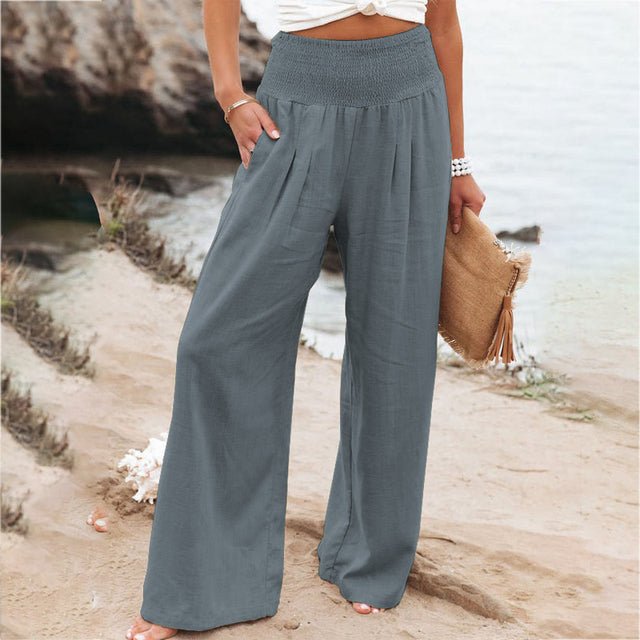 Pantalon large gris femme, taille haute, plage, été, mode décontractée, bord de mer, tenue élégante, accessoire sac paille, style estival.