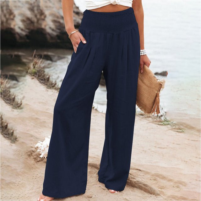 Pantalon large bleu marine femme sur plage, style décontracté estival, accessoire sac en paille, mode plage tendance, tenue confortable.