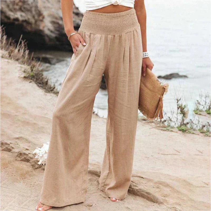 Pantalon large beige en lin pour femme, style décontracté, bord de mer. Mode estivale, tenue élégante et confortable, accessoire sac en paille.