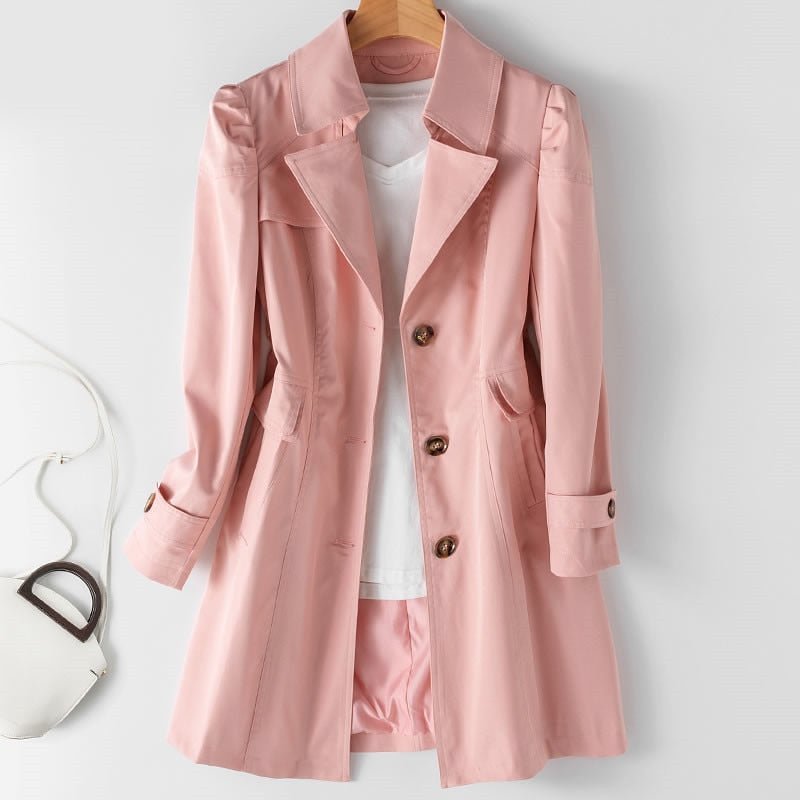 Manteau rose élégant pour femme, accroché sur un cintre, avec boutons marron, chemise blanche en dessous, sac blanc à côté. Mode féminine chic.