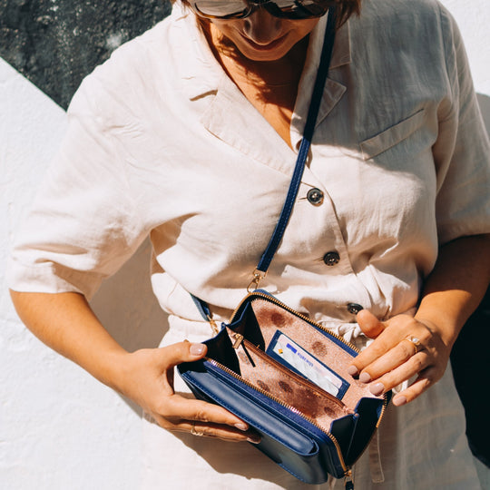 Femme en robe beige tenant un sac à main bleu ouvert, montrant l'intérieur avec une carte visible. Mode estivale, accessoires féminins élégants.
