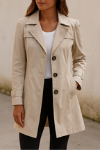 Femme portant un trench-coat beige élégant, manches longues, boutons marron, sur un fond neutre. Mode automne, style classique, tenue chic.