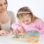 Jeune fille jouant avec un tableau d'activités Montessori en bois, accompagnée d'une femme souriante. Éducation sensorielle, développement enfant.