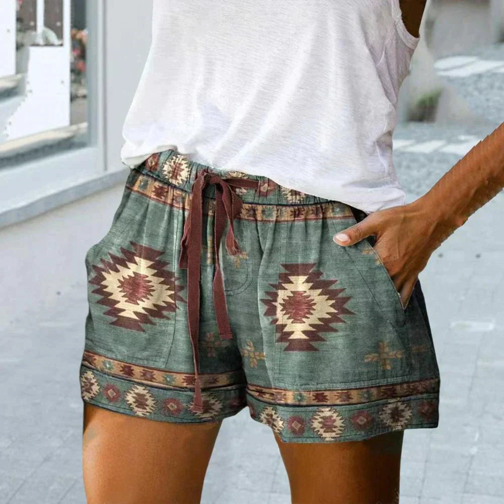 Short en tissu à motifs aztèques verts et marron, avec cordon de serrage, porté par une personne en débardeur blanc. Mode estivale décontractée.