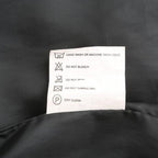 Étiquette d'entretien textile sur tissu noir, indiquant lavage à la main ou machine à froid, ne pas blanchir, repasser, sécher en machine, nettoyage à sec.