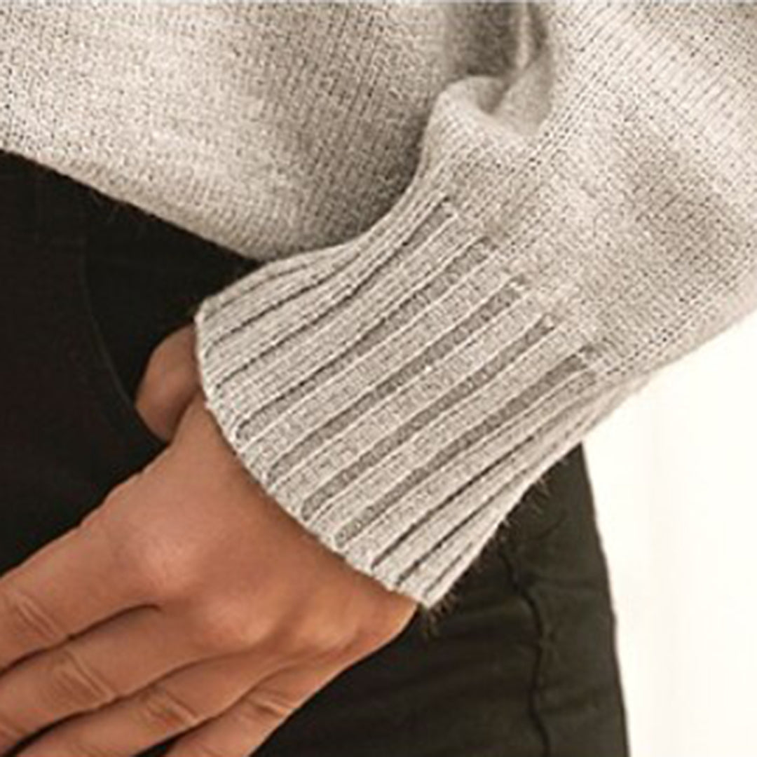 Manche de pull gris en tricot côtelé, main posée sur un pantalon noir. Mode automne-hiver, vêtement chaud et confortable.