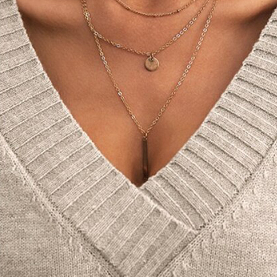 Gros plan sur un pull en tricot gris avec col en V, mettant en valeur des colliers dorés superposés. Mode féminine, accessoires élégants.