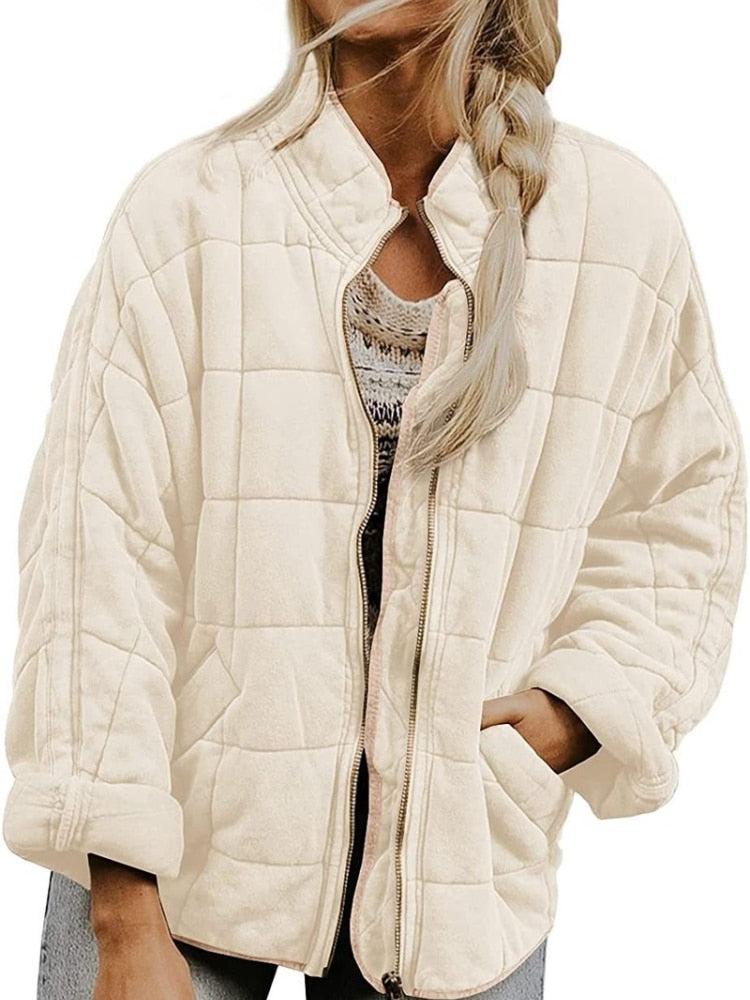 Femme portant une veste matelassée beige, fermeture éclair ouverte, cheveux tressés. Mode automne, style décontracté, tendance vestimentaire.