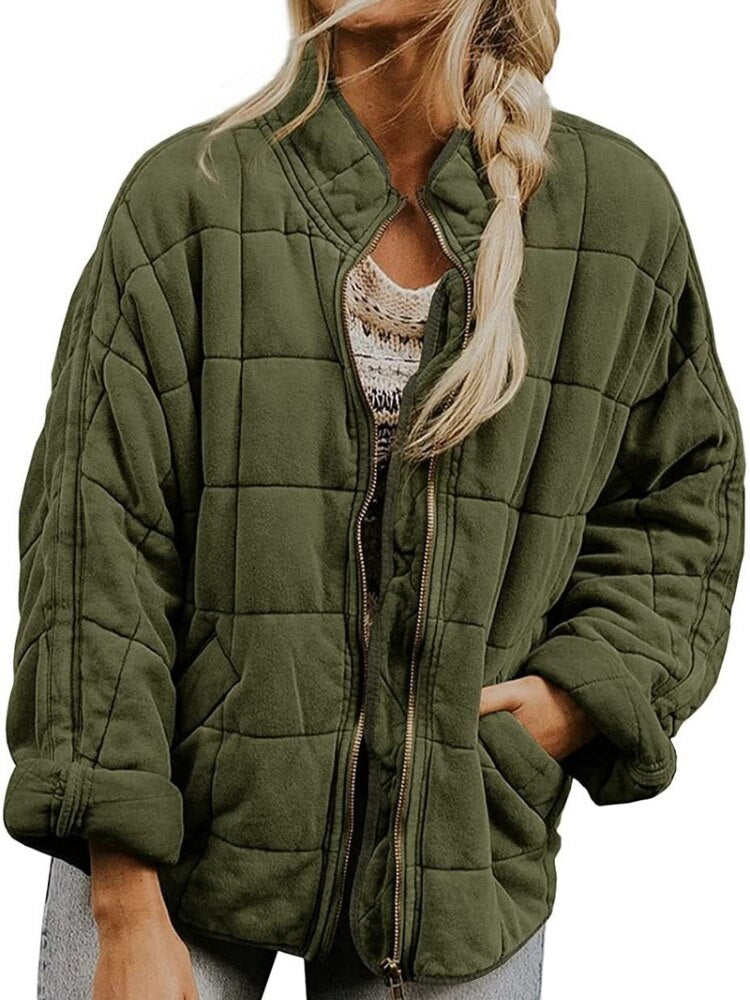 Femme portant une veste matelassée verte, fermeture éclair ouverte, sur un pull beige. Mode automne, style décontracté, tendance vestimentaire.
