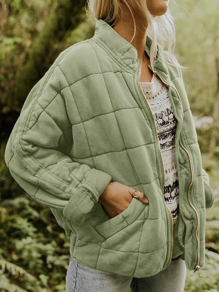 Femme portant une veste matelassée verte, manches retroussées, sur un pull à motifs, en pleine nature. Mode automne, style décontracté.