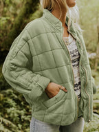 Femme portant une veste matelassée verte, manches retroussées, sur un pull à motifs, en pleine nature. Mode automne, style décontracté.