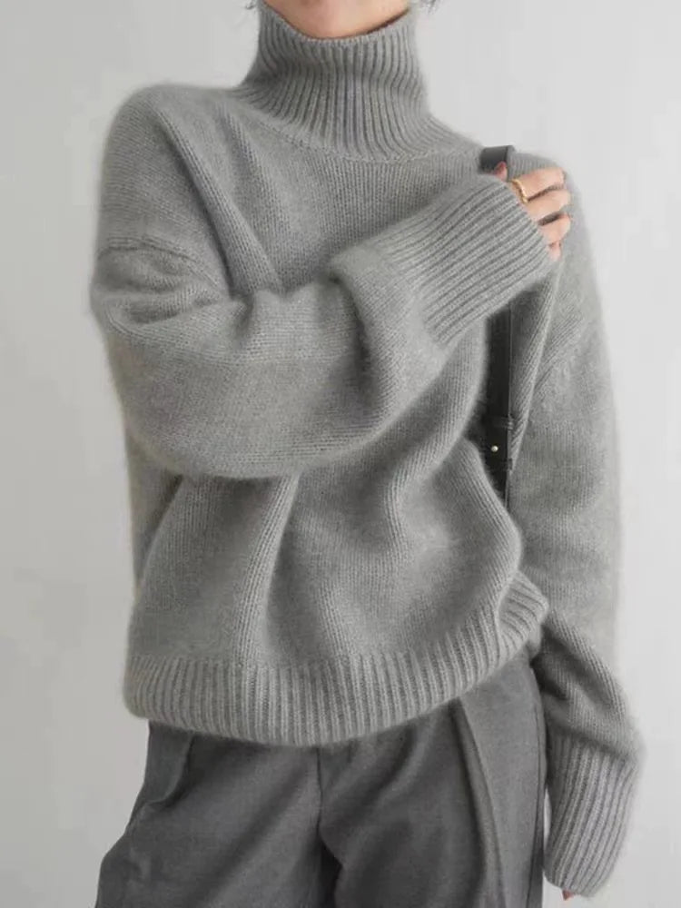Personne portant un pull en laine gris à col roulé, manches longues, associé à un pantalon gris. Mode automne-hiver, style décontracté et élégant.