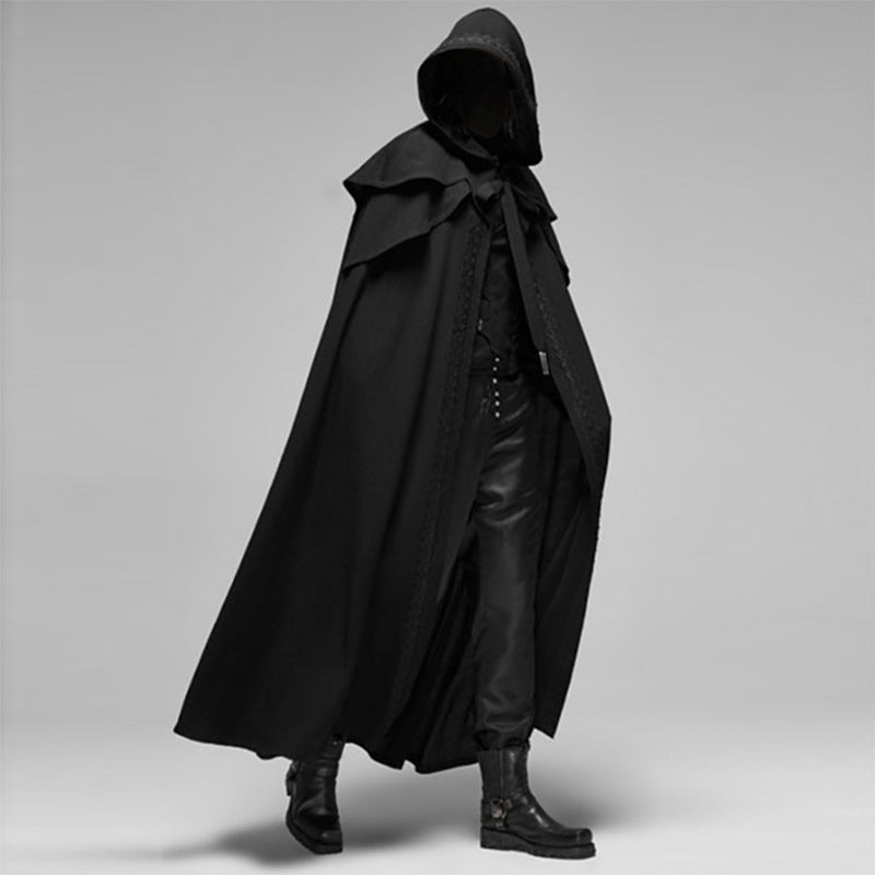Personne en cape noire à capuche, tenue gothique élégante, bottes en cuir, style mystérieux, mode sombre, fond gris.