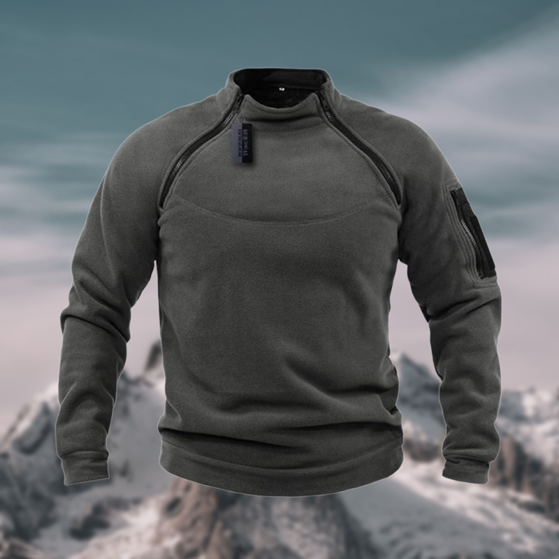 Pull polaire gris foncé pour homme, manches longues, col montant, poche zippée sur la manche gauche, fond montagneux enneigé. Mode hiver outdoor.