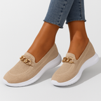 Chaussures beiges en maille avec chaîne dorée, semelle blanche épaisse, portées avec un jean. Style moderne et confortable pour femme.