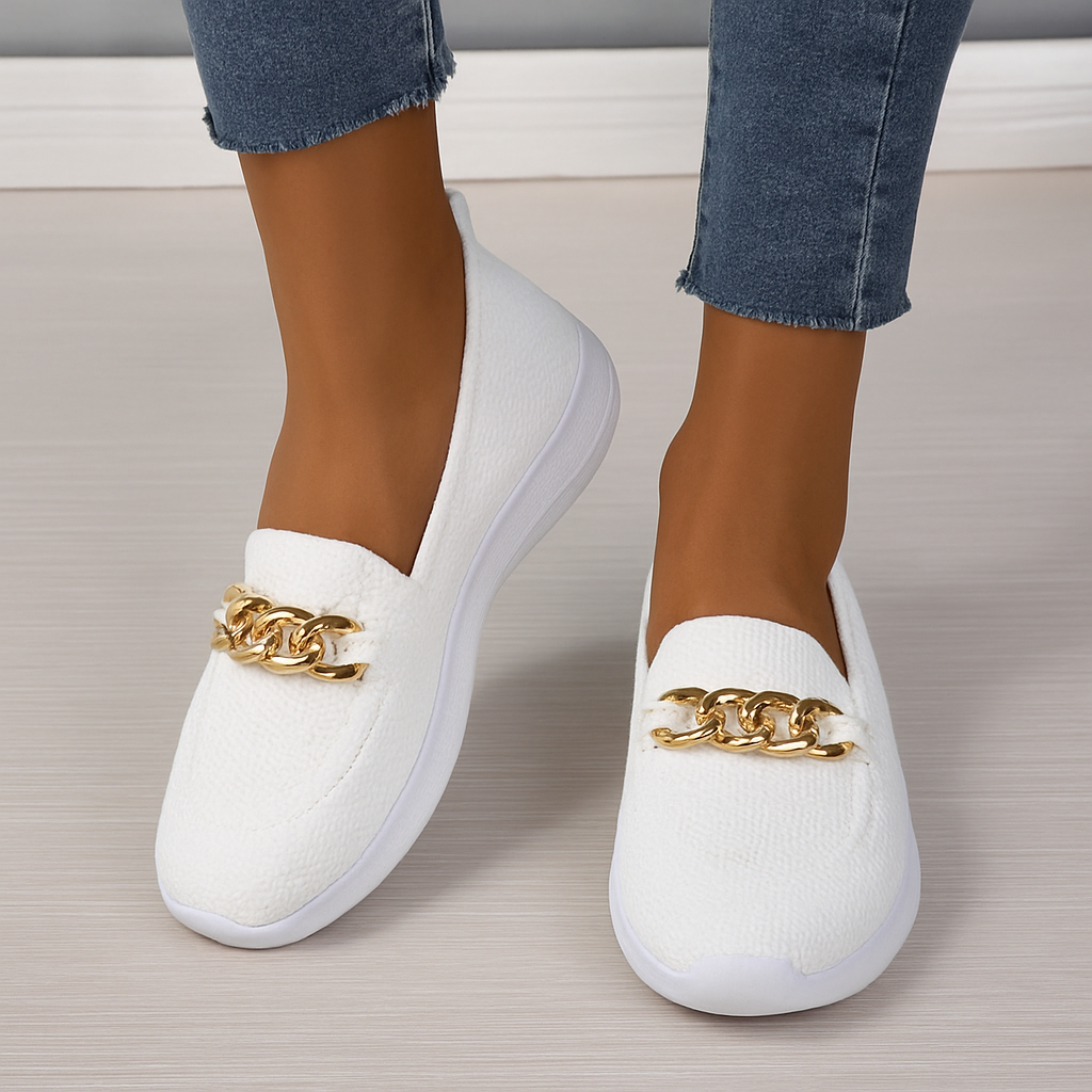 Chaussures mocassins blanches pour femme avec chaîne dorée, portées avec un jean. Style élégant et moderne, parfait pour la mode urbaine.