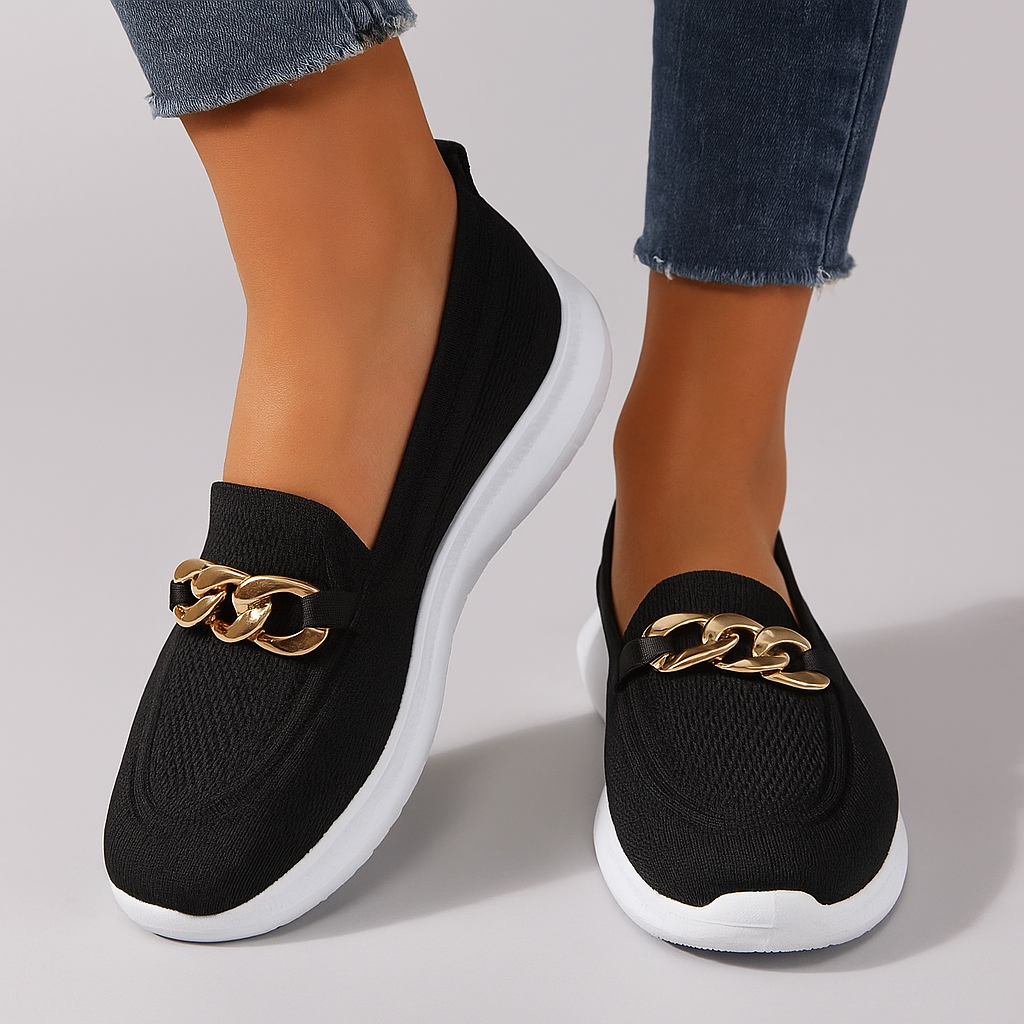 Chaussures noires élégantes avec chaîne dorée, semelle blanche, portées avec un jean. Mocassins tendance pour femme, mode automne 2023.