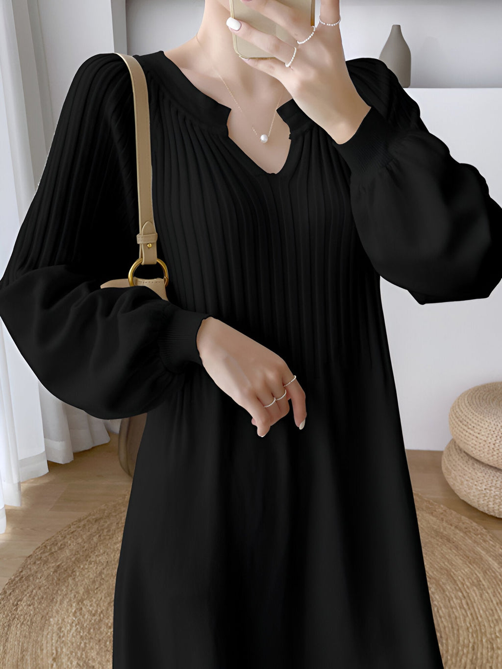 Robe noire élégante à manches longues, plissée, avec sac à main beige. Style chic et moderne, idéal pour la mode féminine automne-hiver.