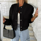 Femme portant un blouson noir tendance, jean décontracté et sac à main noir, posant sur des escaliers en béton. Mode urbaine chic et moderne.
